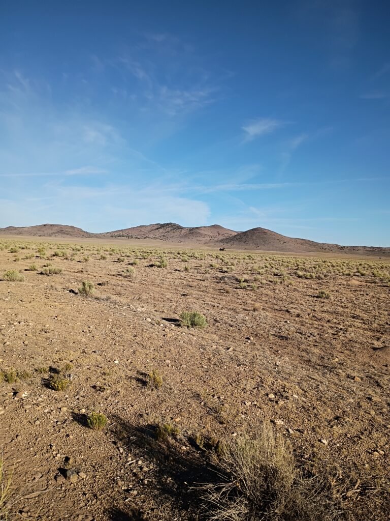 Wide angle view of vast desert sagebrush plains leading to a solitary distant mountain under a partly cloudy sky.